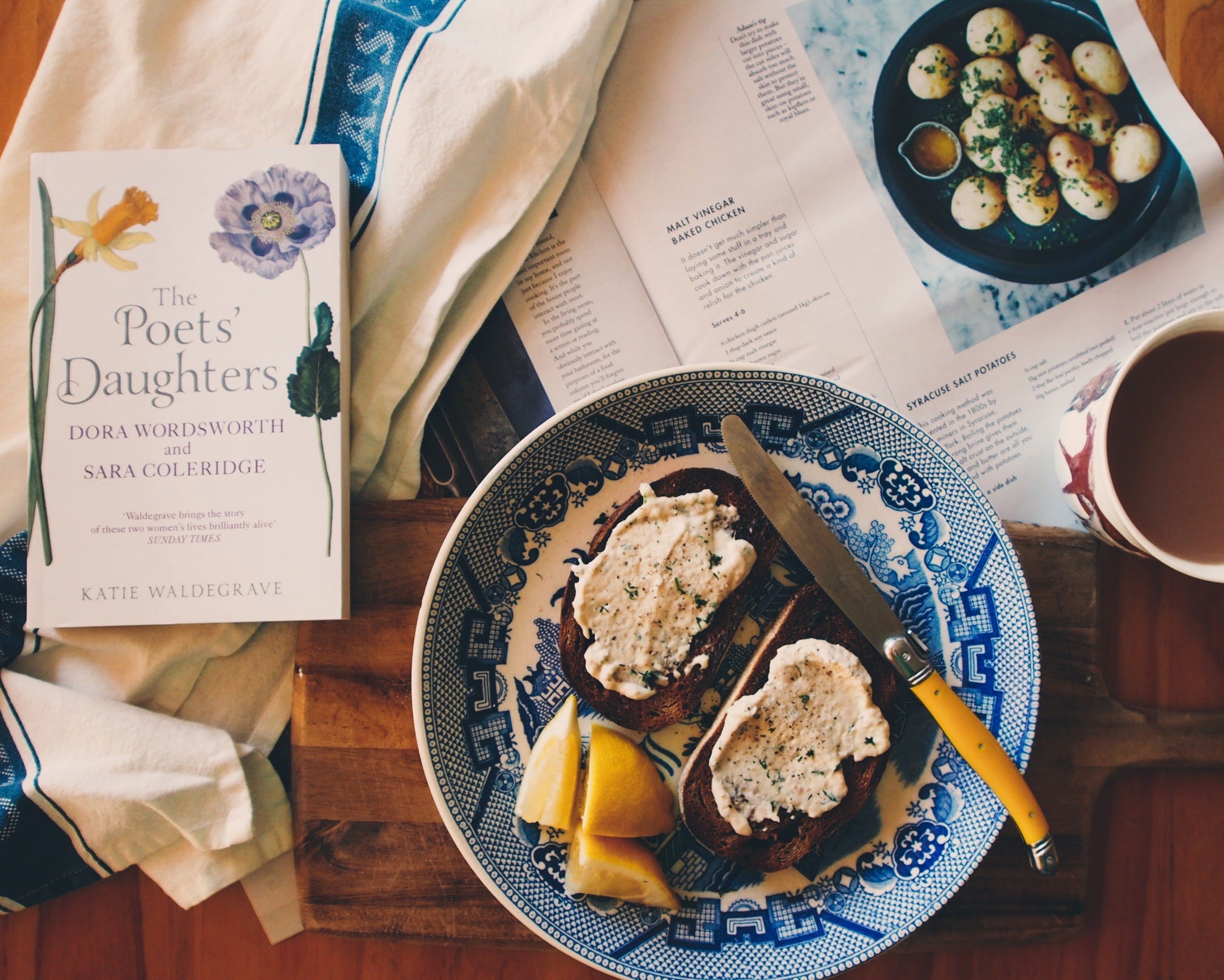 a plate of smoked trout dip on toast, a book called The Poet's daughter, a cup of tea and the Sunday magazine