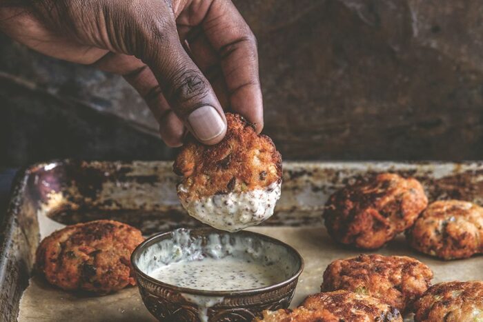 A hand dipping a salmon croquette into remoulade