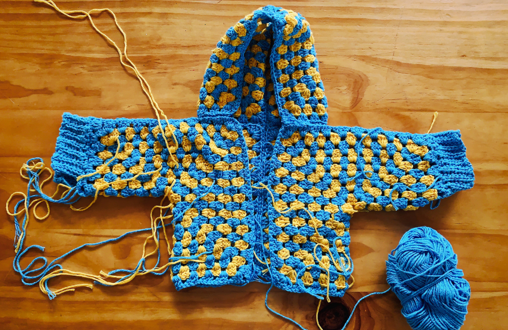 An in-progress yellow and blue crocheted jacket for baby June.