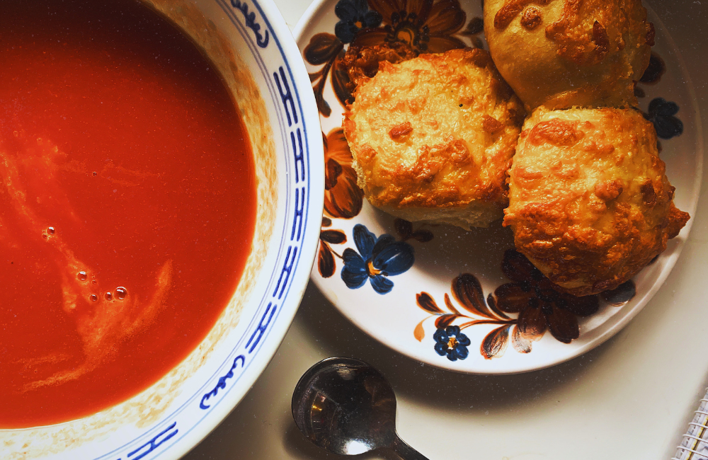 A bowl of tomato soup and a plate of 3 mini cheese and bacon rolls