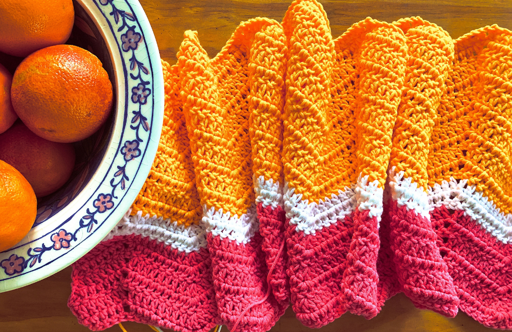 Pip's Cheery Wave Ripple crocheted blanket in pink, yellow and white, alongside a decorated bowl of blood oranges