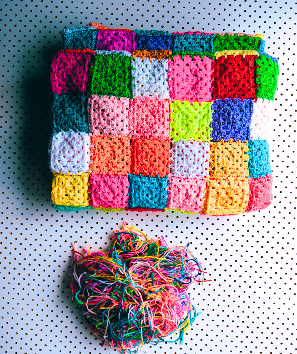 Colourful granny square crocheted blanket beside a pile of loose wool ends which have been clipped from the blanket.