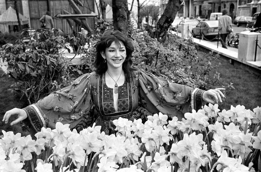 Kate Bush arms outstretched over bunches of daffodils. Image is black and white.