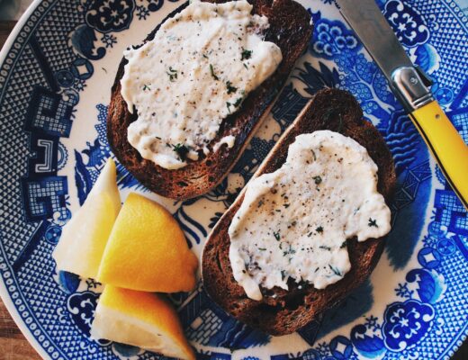 a plate with two slices of scorched toast slathered with smoked trout dip, there are some lemon segments and cutlery too