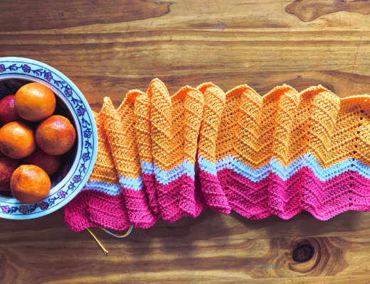 A yellow, pink and white ripple blanket on a tabletop alongside a bowl of blood oranges